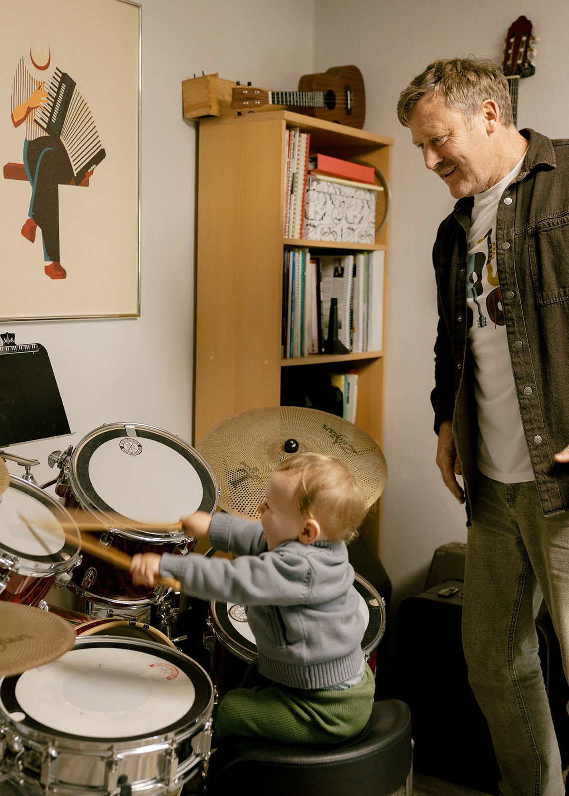 Ein Kind spielt am Schlagzeug, Willi Wiebe beobachtet lächelnd.