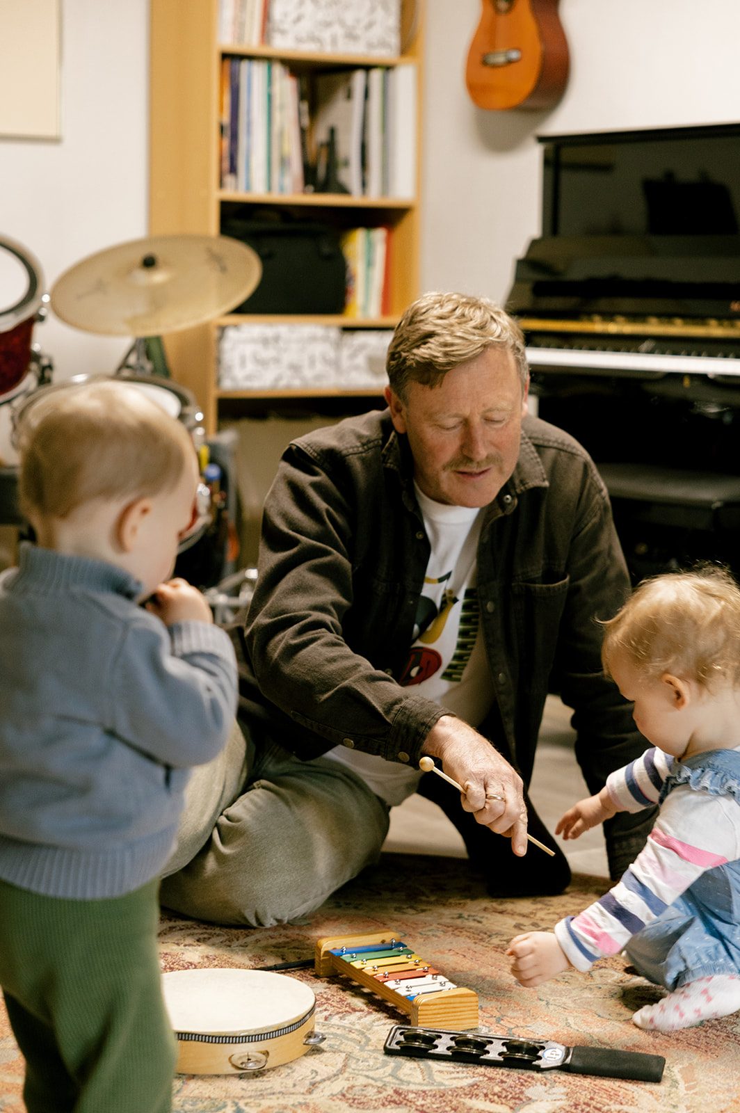 Willi Wiebe mit zwei kleinen Kindern an Xylophon und Trommel – musikalische Früherziehung im Musikzimmer.